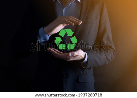 Businessman in suit over dark background holds an recycling icon, sign in his hands. Ecology, environment and conservation concept. Neon red blue light.