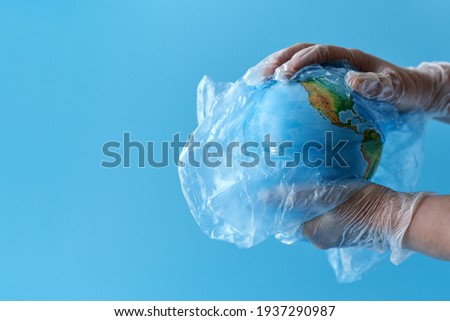 Hands hold a globe in a plastic bag on a blue background. Copy space.                               
