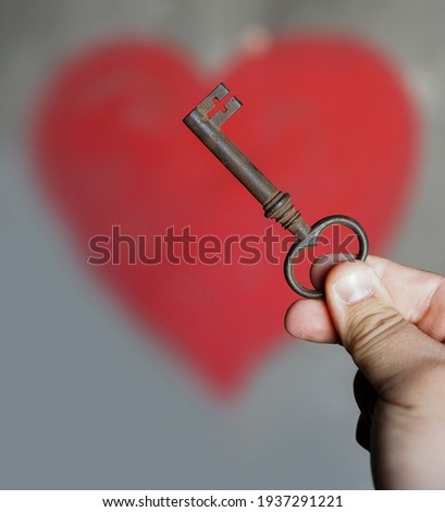 male hand holding old vintage key on wall background with red heart.