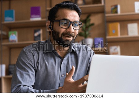 Indian business man speaking having virtual meeting on laptop. Professional remote online customer service support manager wearing headset talking consulting on video call at home office call center. Royalty-Free Stock Photo #1937300614