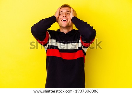 Young caucasian man isolated on yellow background laughs joyfully keeping hands on head. Happiness concept.