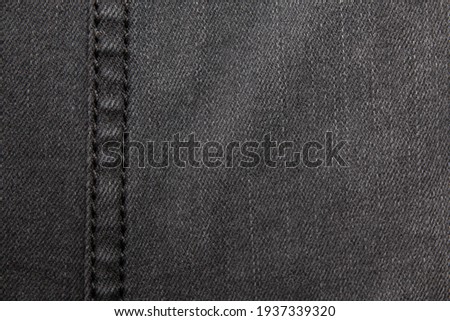 Black denim with stitching details. Background on the theme of denim clothing.