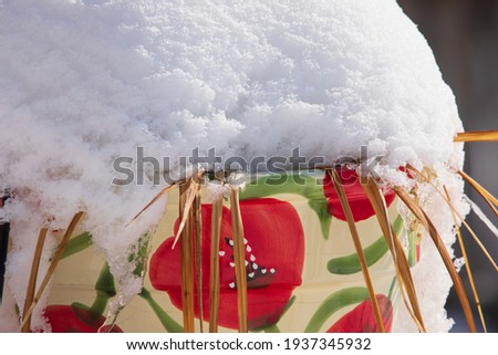 Snow covered flower pot with snow build up around it.  Drifted snow on top of large floral flower pot.   Royalty-Free Stock Photo #1937345932
