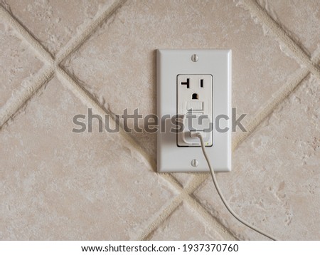 USB cell phone power adapter brick and cord in GFCI wall plug. Electrical cord and charger plug in wall outlet. Royalty-Free Stock Photo #1937370760