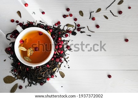 Tea leaves with lingonberry berries and a cup of tea on a white background with space for text. The concept of a healthy drink. Royalty-Free Stock Photo #1937372002
