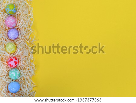 Colorful Easter eggs on paper shavings egg side border against yellow background. Eggs painted by a child. Flat lay style, copy space