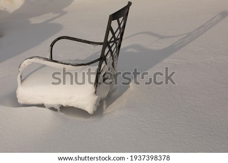 Outdoor patio furniture left out in the snow.  Summer furniture covered with fresh snow.  Snow drifted over patio furniture