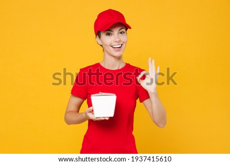 Delivery employee woman in red cap blank t-shirt work courier in service during quarantine coronavirus covid-19 virus holding Chinese food takeaway carton container box isolated on yellow background