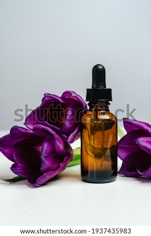 Massage oils in a dark glass jar. Essence for skin health. Trendy style. Mockup for your product. Conceptual photo. 
Aroma Oil and tulips on a white background.
