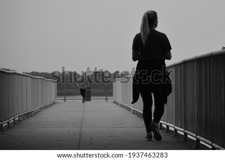 A woman looking out at the water as a child runs towards her.
