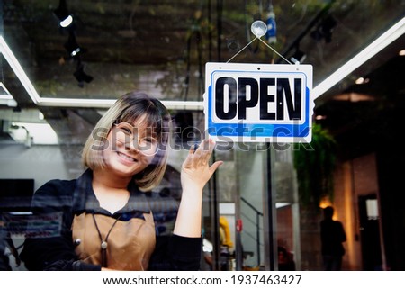 
Asian female hairdesser of salon shop turning round open sign on a door. 
