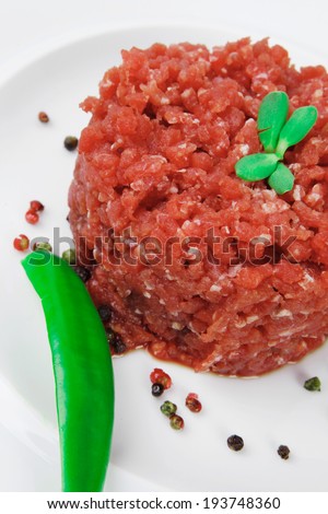 very big raw hamburger cutlet with sprouts and chilli pepper on white plate isolated over white background
