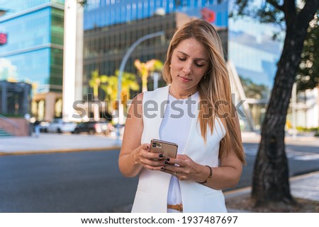 Successful businesswoman texting with her cell phone while walking down the street on a beautiful afternoon