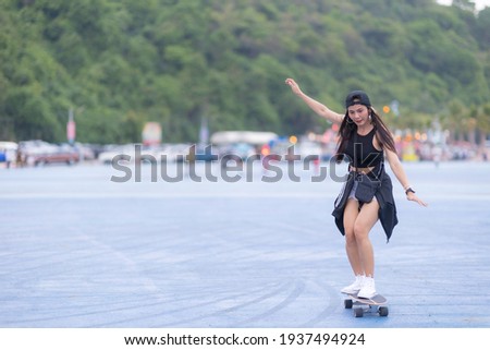 Asian woman playing surf skate or skates board outdoors on beautiful summer day. Happy young women play surf skate at park on morning time in the park. Royalty-Free Stock Photo #1937494924