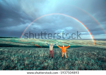 two elderly men raised their hands up and rejoice beautiful big rainbow spring day