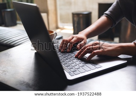Closeup image of a woman working and typing on laptop computer keyboard on wooden table Royalty-Free Stock Photo #1937522488