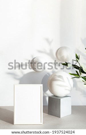 Mock-up poster frames in the interior of geometric shapes. Contemporary still life scene in neutral colors with an olive branch. Minimal composition with white photo frame and interesting shadows