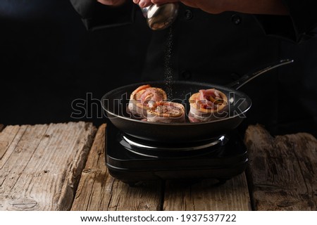 Chef prepares meat steaks in bacon, beef or pork. Chef on black background for restaurant menu text copy space