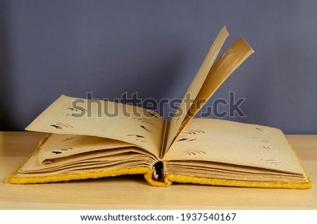 An open old photo album wrapped in yellow velvet. Vintage photo album with blank pages against a gray wall. Side view at an angle.