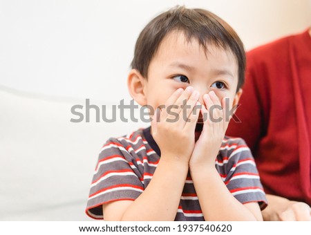 Asian toddler little boy covering face with both hands being afraid of watching scary movie.Confused timid child feeling shy hiding his emotions.Allergy, Sad, mask, no food, Bad breath, guilty, Repent