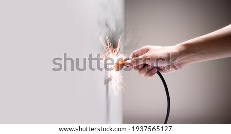 Hand connecting electrical plug cause electric shock, Idea for causes of a home fire, Electric short circuit, Electrical hazard can ignite household items, Residential building electrical fires. Royalty-Free Stock Photo #1937565127
