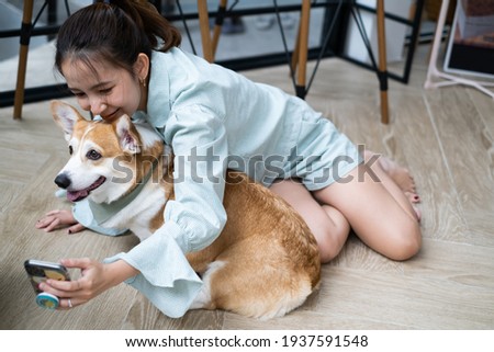 Curly woman playing with corgi pappy. Cheerful young lady smiles and sits on wooden floor selfie by phone camera with dog. love pet best friend and family concept