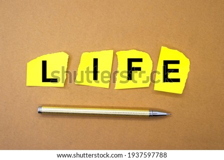A yellow sheet of paper is torn into four pieces each with a black letter representing the word life.