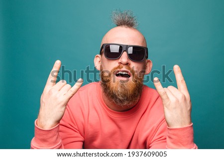 Bearded european man in casual peach isolated on turquoise background  shouting with crazy expression doing rock symbol with hands up