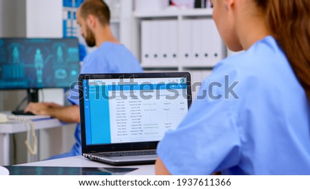 Professional doctor assistant checking medical records on laptop with x-ray and medical equipment around. Physician working in hospital clinic making appointments and analysing patient registration Royalty-Free Stock Photo #1937611366