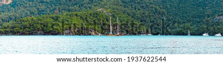 Summer concept: A Turkish gullet and behind some luxury white yachts anchored at the Aegean sea with sun beam in background. Natural photo with copy space. Green and blue contrast. No people