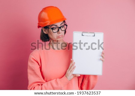 Sad unhappy disappointed woman worker builder hold white sign board blank against pink background. Building helmet.