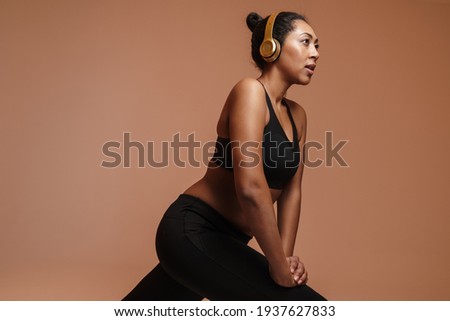 Confident focused afro american excited sportswoman isolated over pink background, listening to music with headphones while exercising