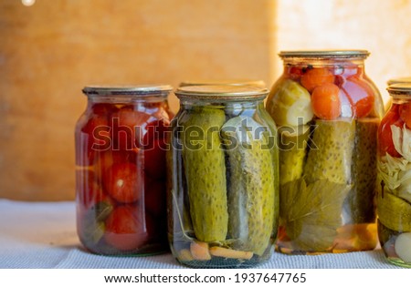 Glass jars with pickled cucumbers (pickles), pickled tomatoes and cabbage. Jars of various pickled vegetables. Canned food in a rustic composition. Royalty-Free Stock Photo #1937647765