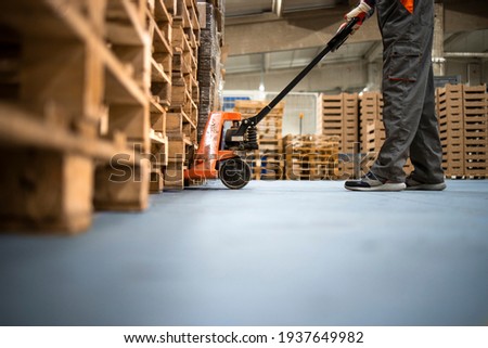 Working at warehouse. Low angle view of unrecognizable worker lifting palette with manual forklift. Royalty-Free Stock Photo #1937649982