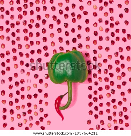 Arrangement of green paprika with red chili and pomegranate seeds. Taken from above on pastel pink background.