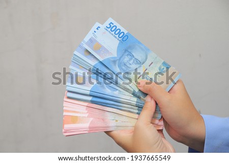 woman's hand showing rupiah banknotes on white background. IDR 100000  and IDR 50000 Royalty-Free Stock Photo #1937665549