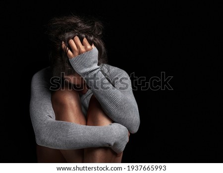 Depression or domestic violence concept: Sad lonely young woman crying while sitting in dark room with an attitude of sadness and boredom with her legs together and hugged. Royalty-Free Stock Photo #1937665993