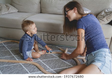 Little kid boy and his mother playing with railway sitting on the floor.