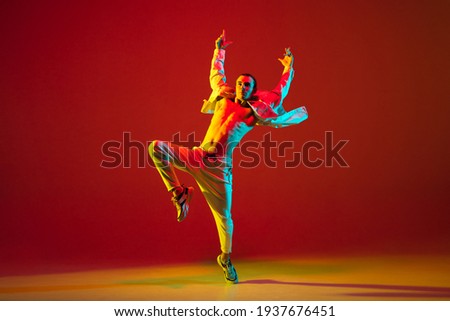 Modern dance. Hip-hop male dancer athletic man dancing in stylish white attire isolated over colorful background in red neon light. Youth culture, fashion, action, freestyle. Copy space for ad