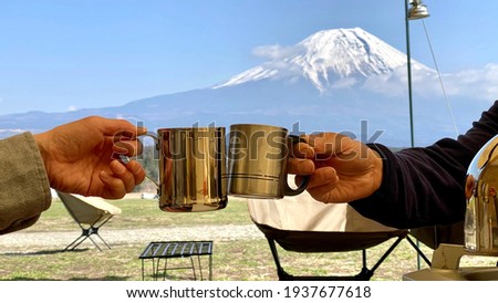 Two hands toasting with a stainless mug in front of Mt. Fuji