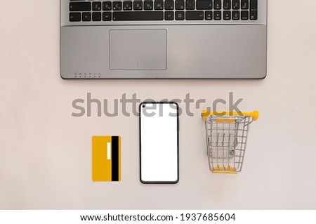 Smartphone with white screen mockup, laptop, yellow credit card, shopping trolley. Online shopping concept, online shopping applications, discounts, black friday. view from above. Flat lay. copy space