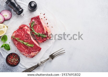 Two raw steak New York with rosemary and spices on black stone cutting board on light white stone background.  Top view. Mock up.