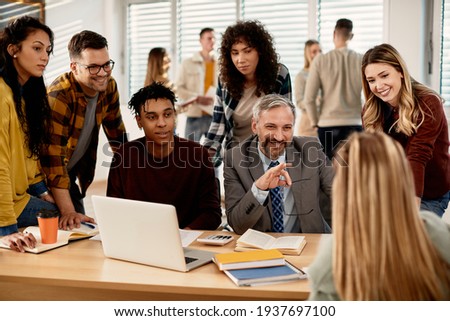 Happy mature professor communicating with group of college students in the classroom.  Royalty-Free Stock Photo #1937697100