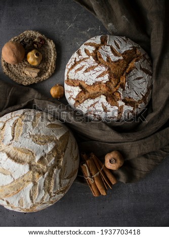 Still life with two artisan breads, linen towel, cinnamon sticks, dried fruits and silver knife. Grey textured background. Healthy eating concept. 