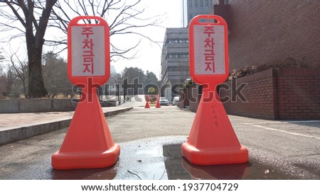 Translated from Korean as "No Parking", two traffic cones and two others at the distance prevent parking on this street.