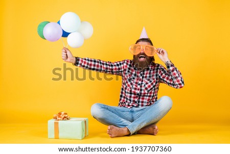 Relaxed happy birthday guy looks cheerful. bearded man feel the joy. man with gift box celebrating birthday. mature hipster with bright colorful balloons. Crazy funny guy