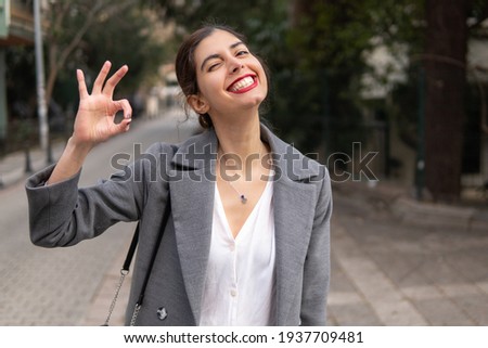 Happy Arabic businesswoman with a smile and ok sign in red lipstick on the street 