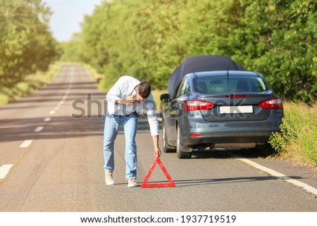 Young man with emergency stop sign near broken car on road