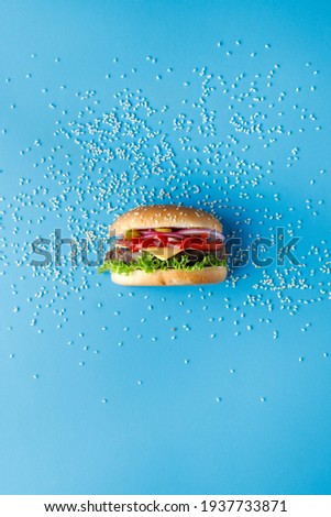 Burger with sesame seeds laid out around on blue backdrop. Creative colorful burger