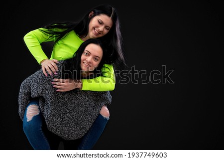 two girlfriends having fun, one carries the other on her back and laughs, isolated on black background